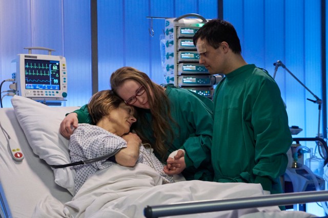 Carina Kühne als Manja Jokisch am Krankenbett von Karin Giegerich als Mutter und Addas Ahmad als Freund in grünen Krankenhauskitteln,